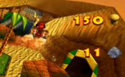 Diddy Kong usando el movimiento (volando y disparando) en Donkey Kong 64. Al lado están la cantidad de cacahuates/cacahuetes y cocos de cristal restantes.