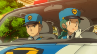 Un policía con la oficial Jenny/agente Mara en un coche patrulla, alertando a la ciudad.