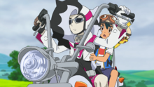 Piers/Nerio en su moto junto a Ash.